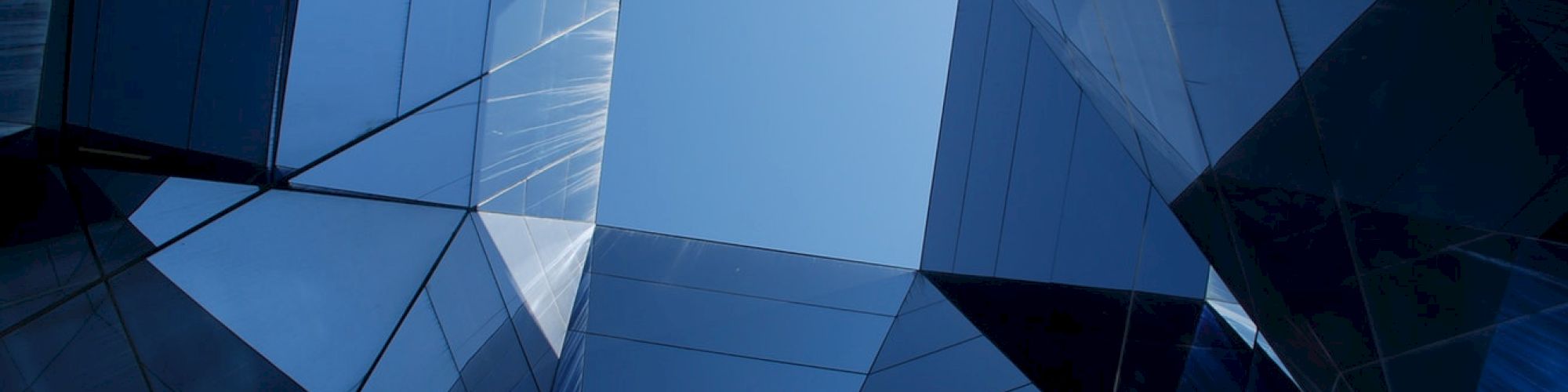 The image shows a perspective view looking up at a geometric pattern formed by the reflective glass surfaces of a modern building, revealing the sky.