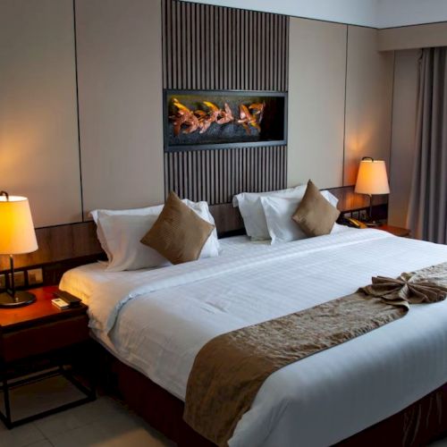 A cozy hotel room featuring a large bed with two pillows, bedside tables with lamps, a fireplace, and window with curtains.