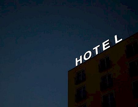 The image shows a building with a partially lit "HOTEL" sign against a dark sky, where the "L" appears to be detached from the sign.