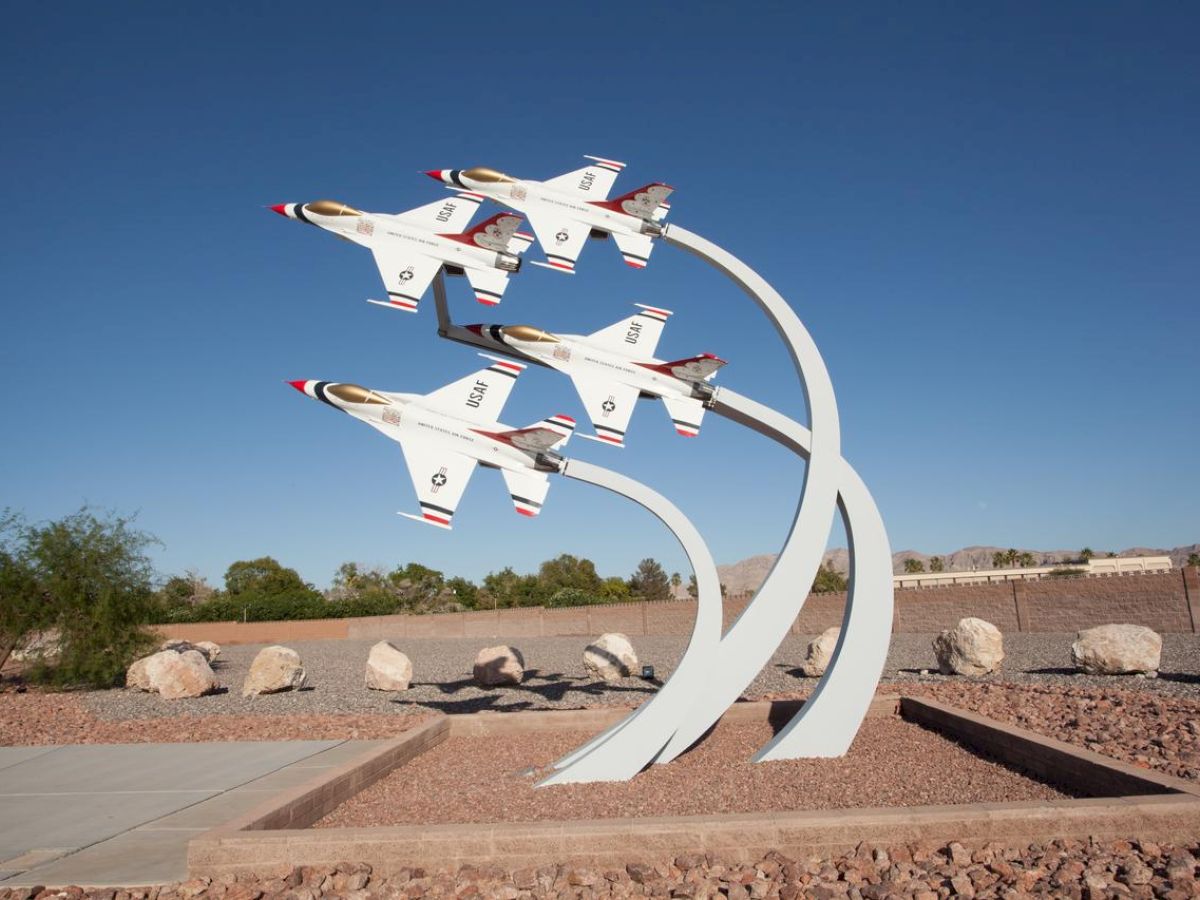 A statue of four jets flying in formation is displayed outdoors with a clear sky backdrop.