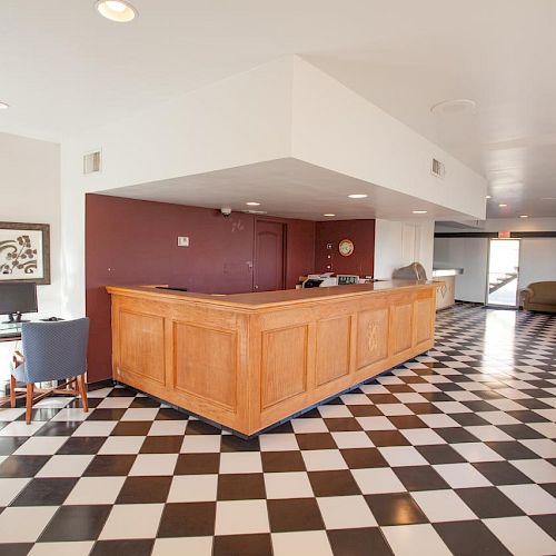 The image shows a reception area with a wooden check-in counter, black and white tiled floor, and seating area with chairs and a sofa ending the sentence.