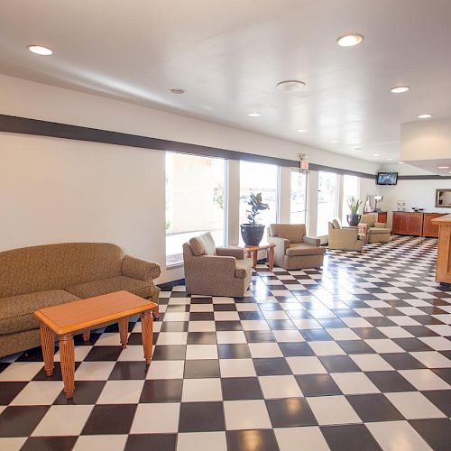 The image shows a lobby area with black and white checkered flooring, seating, coffee tables, and a reception desk in the background.