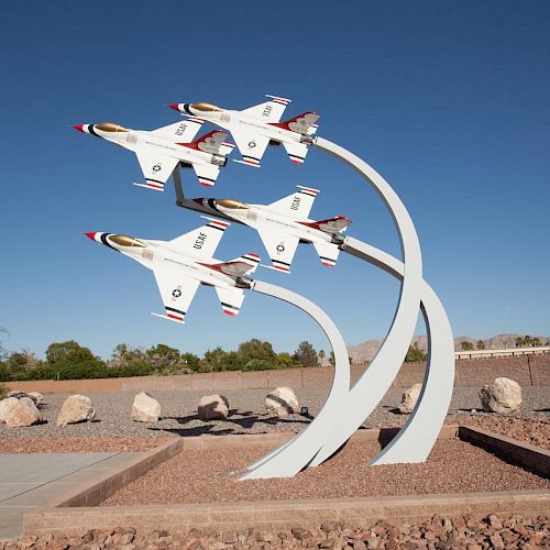 The image shows a public display featuring four model jet planes arranged in a flying formation, mounted on curved supports in an outdoor setting.