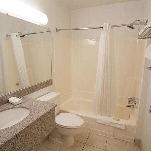 This is an image of a clean, modern bathroom with a sink, mirror, toilet, bathtub, shower curtain, towel racks, and towels neatly arranged.