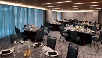 The image shows an elegant banquet hall set up with round tables, each decorated with black and white table settings and floral centerpieces.