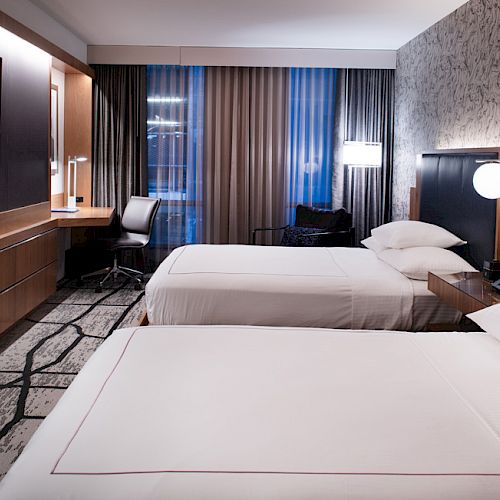 A modern hotel room with two neatly made beds, a wall-mounted TV, a work desk, and stylish decor with patterned wallpaper and carpet ending the sentence.