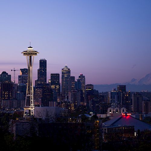 This image shows the Seattle skyline at dusk, featuring the Space Needle prominently and Mount Rainier in the background, under a twilight sky.