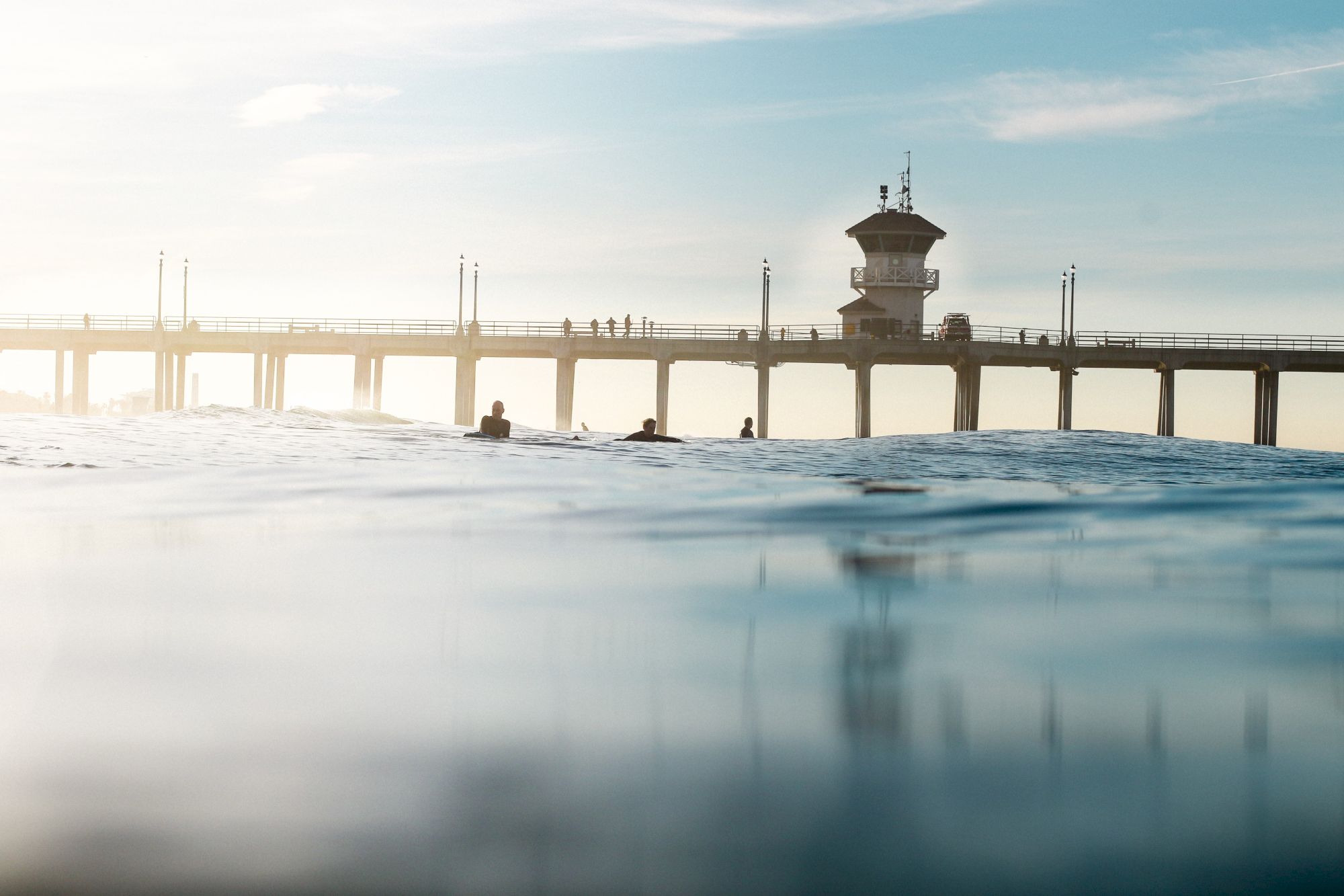 A serene ocean view with a pier extending over the water, silhouetted figures, and a clear sky in the background.